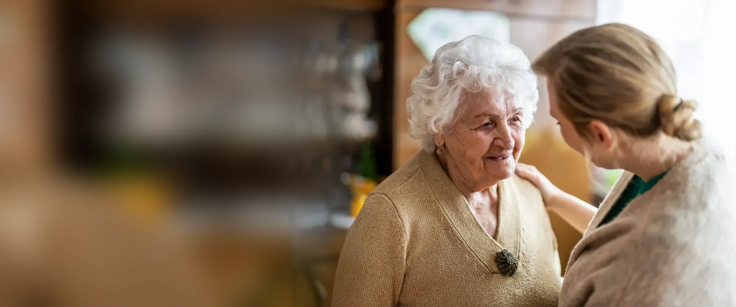 Pflegerin legt einer Seniorin zu Hause die Hand auf die Schulter – 24-Stunden-Pflege