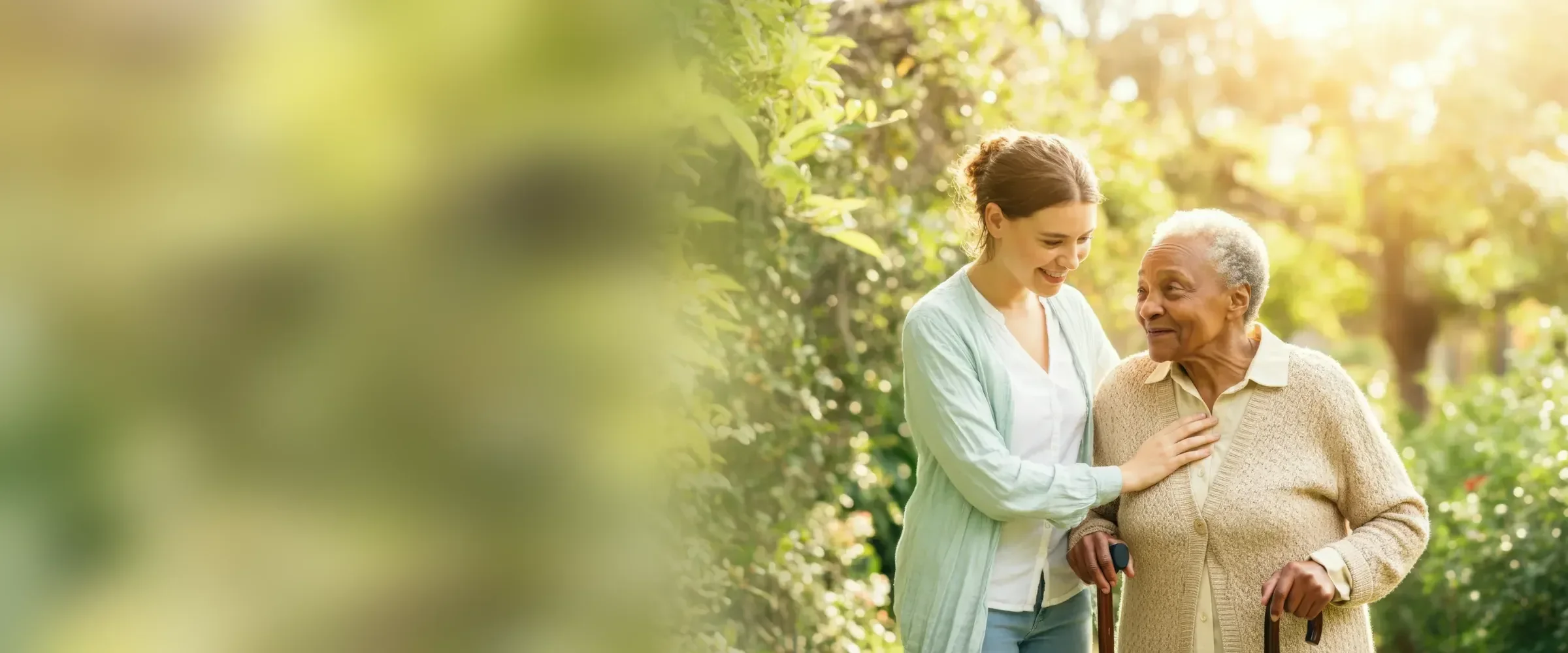 Pflegerin begleitet eine Seniorin mit Gehstock beim Spaziergang im Garten