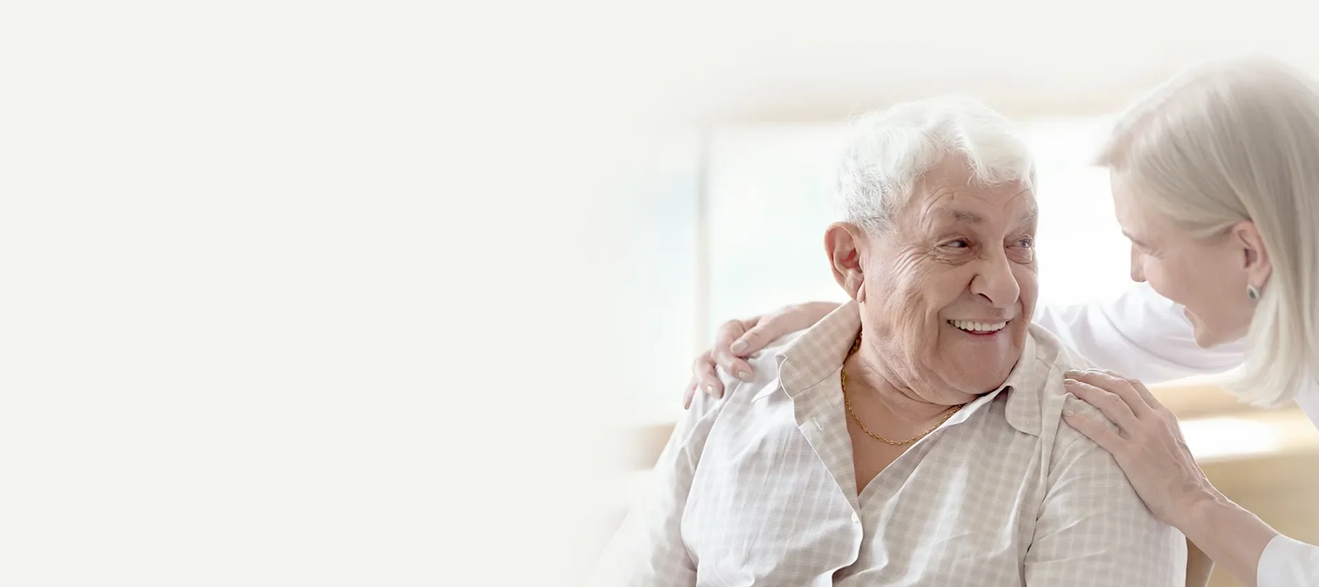 Lächelnder Senior wird zu Hause liebevoll begleitet